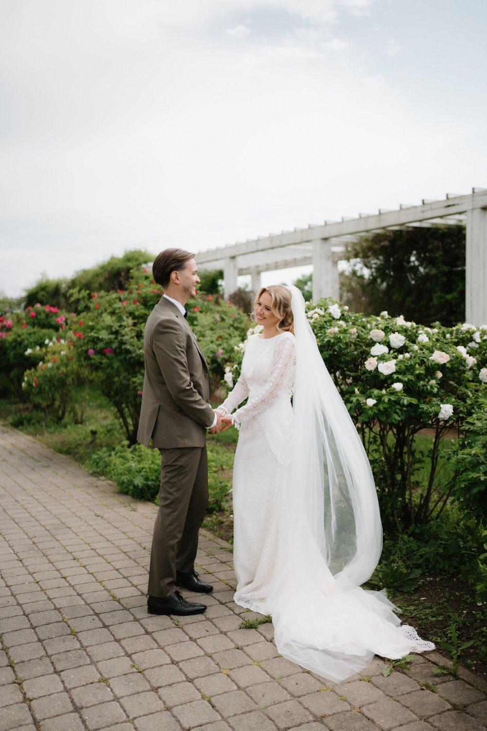 Wedding couple sharing a moment together in a rose garden with white pergola.