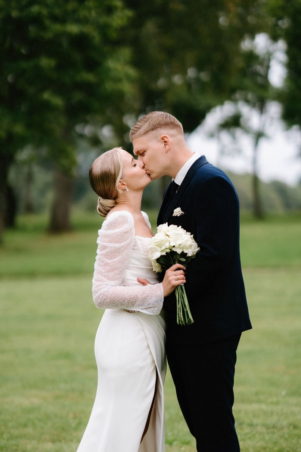 A romantic moment between newlyweds in a park setting with the bride holding a white bouquet.