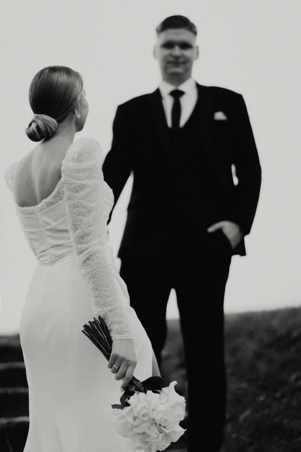 High contrast black and white portrait of newlyweds on stone steps with dramatic lighting.