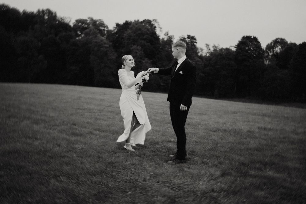 Black and white photo of newlyweds sharing a joyful moment in an outdoor setting.
