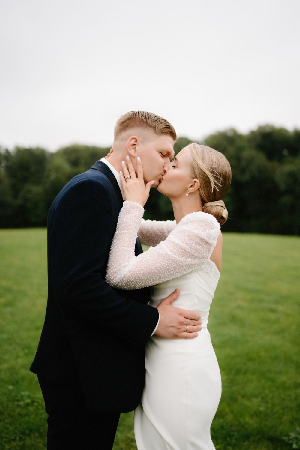 Romantic wedding couple embracing in a green field wearing classic white dress and dark suit.