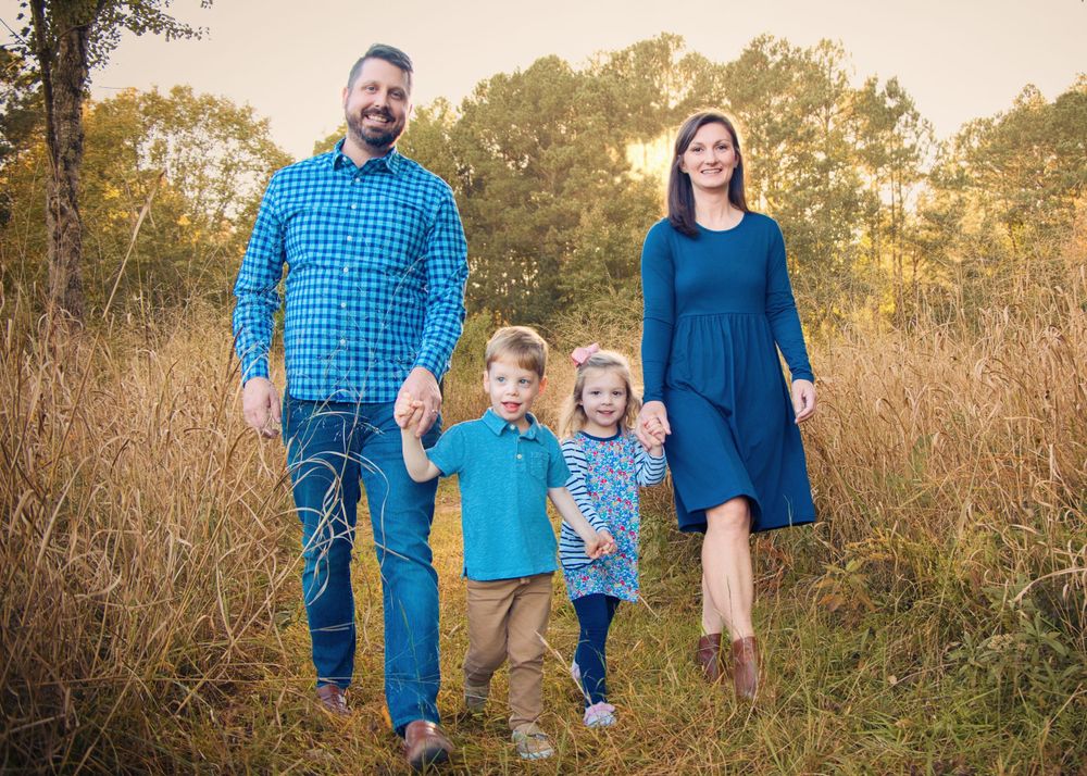 Family of four walking together through tall grass during golden hour.
