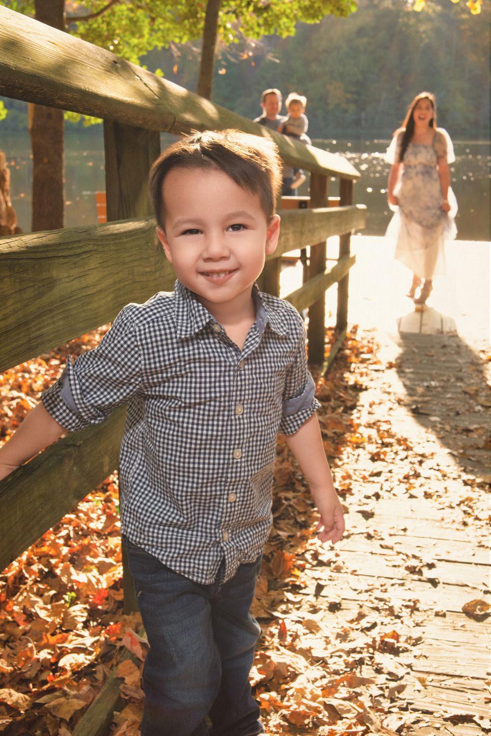 Child walking on wooden boardwalk covered in autumn leaves on sunny day.
