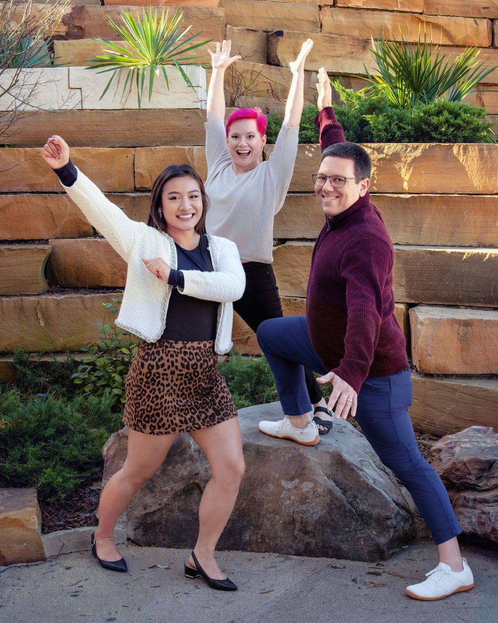 Three friends posing energetically on stone steps with succulent garden background.