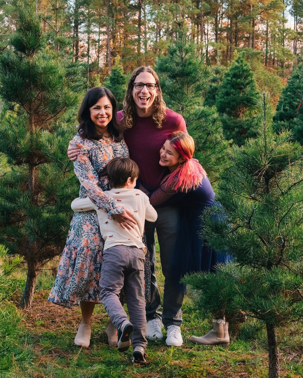 Group poses together among evergreen trees at festive outdoor holiday photoshoot.