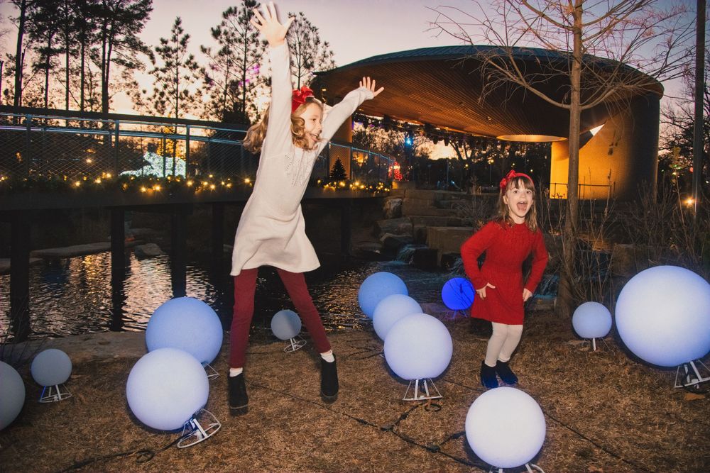 White balloons decorate a twilight garden scene with figures playing and jumping near a covered structure.