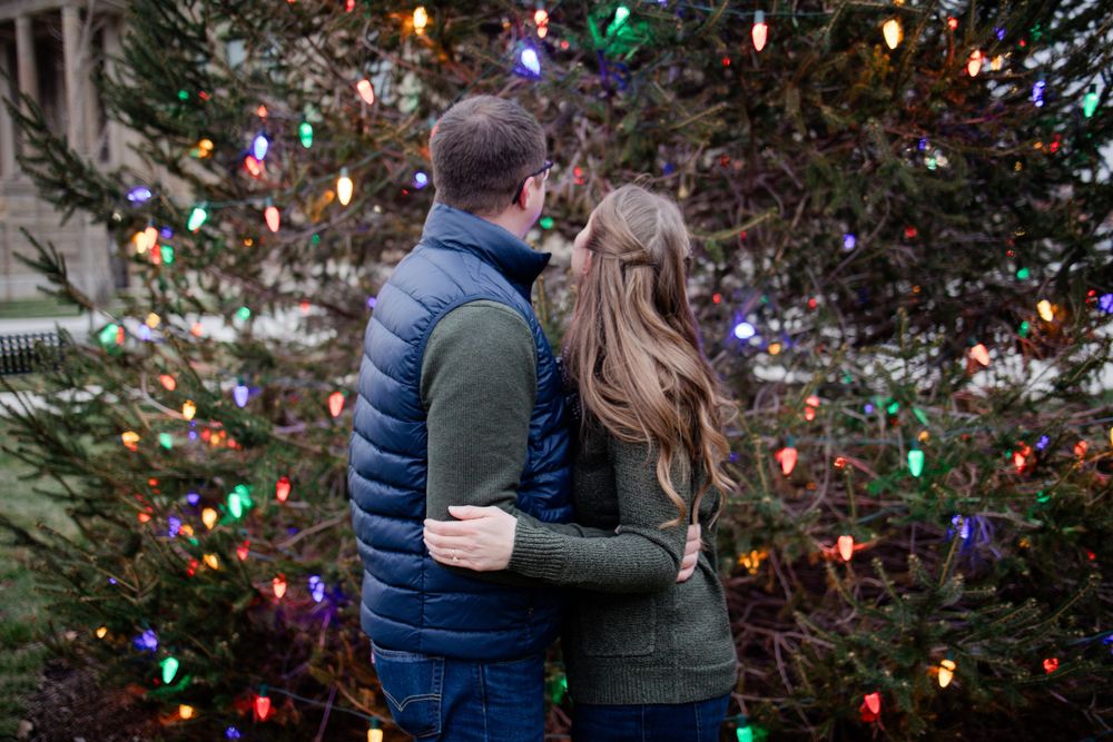A couple embraces near a decorated Christmas tree with colorful lights at night.