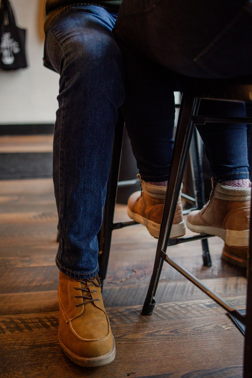 Person wearing blue jeans and brown leather boots sitting at a wooden bar stool.