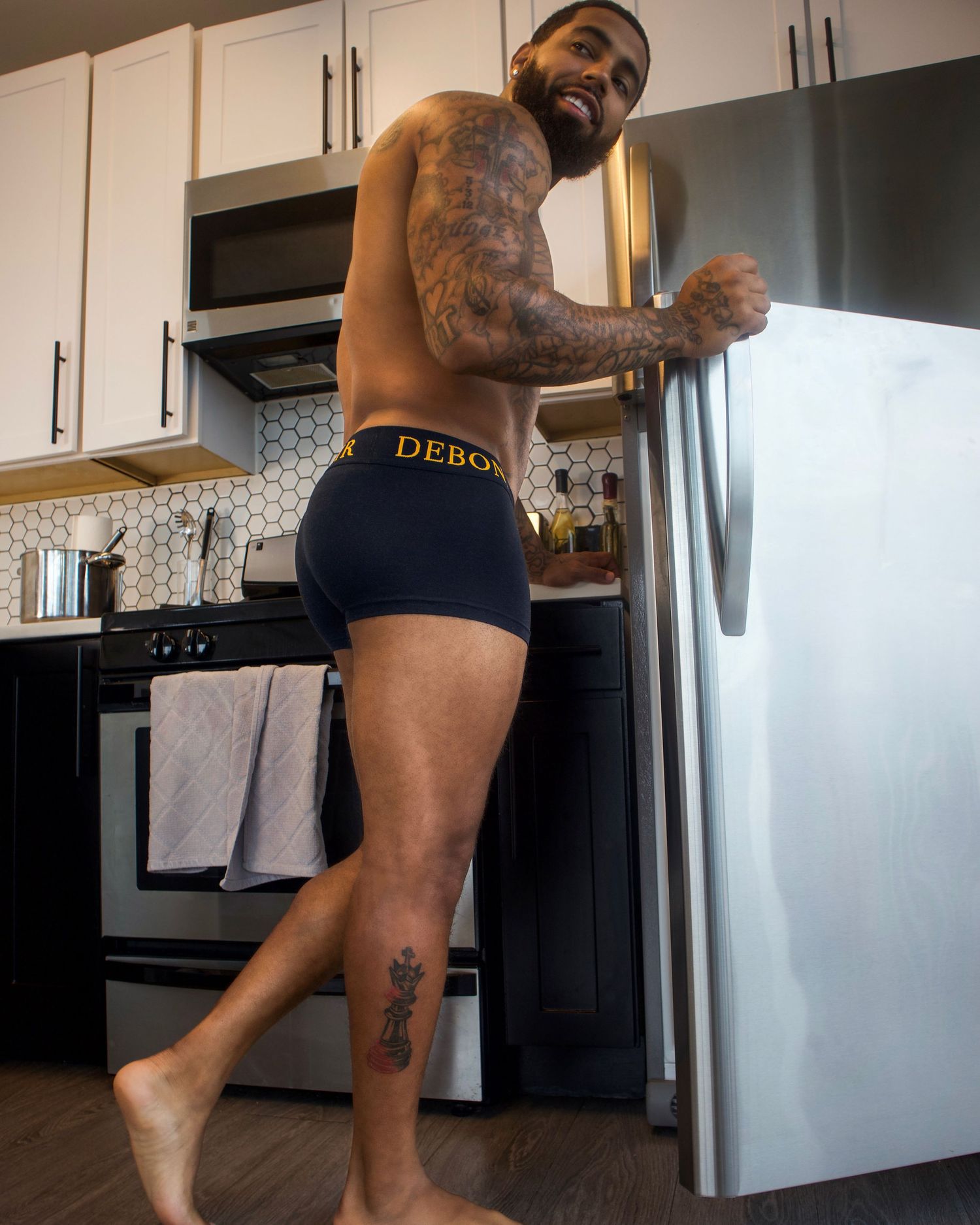 A person wearing navy blue boxer briefs stands barefoot in a modern kitchen with stainless steel appliances.