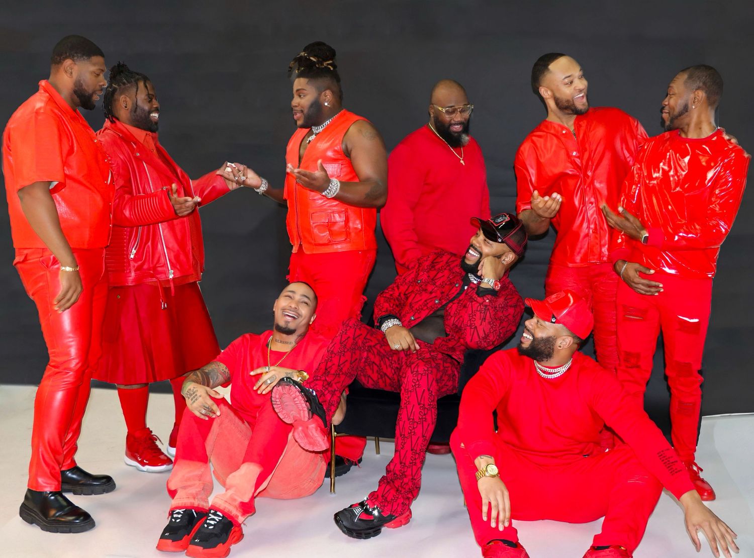 Group poses together wearing coordinated bright red outfits against dark background in stylized photoshoot.