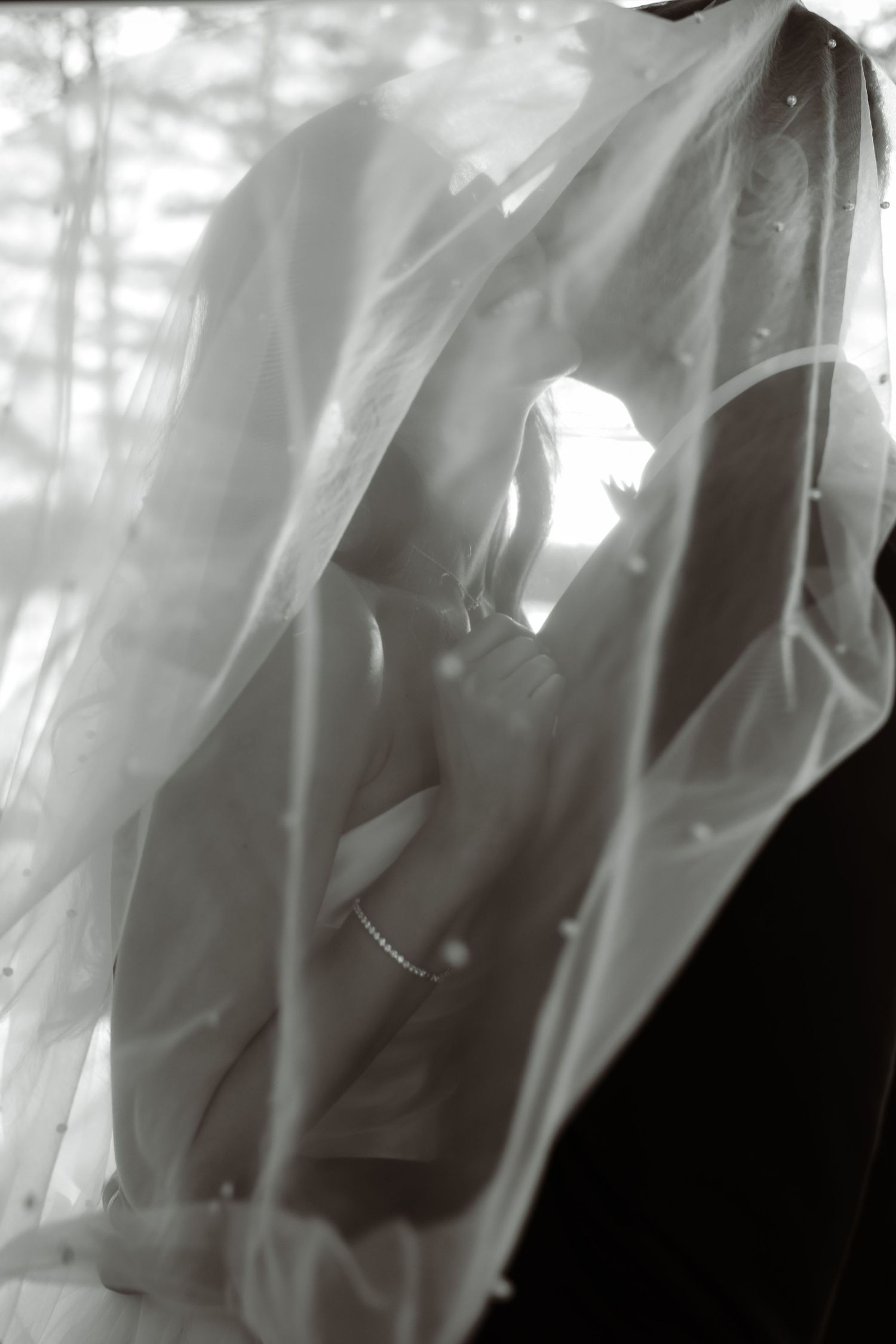 Artistic black and white photo showing silhouette of wedding dress details through sheer fabric.