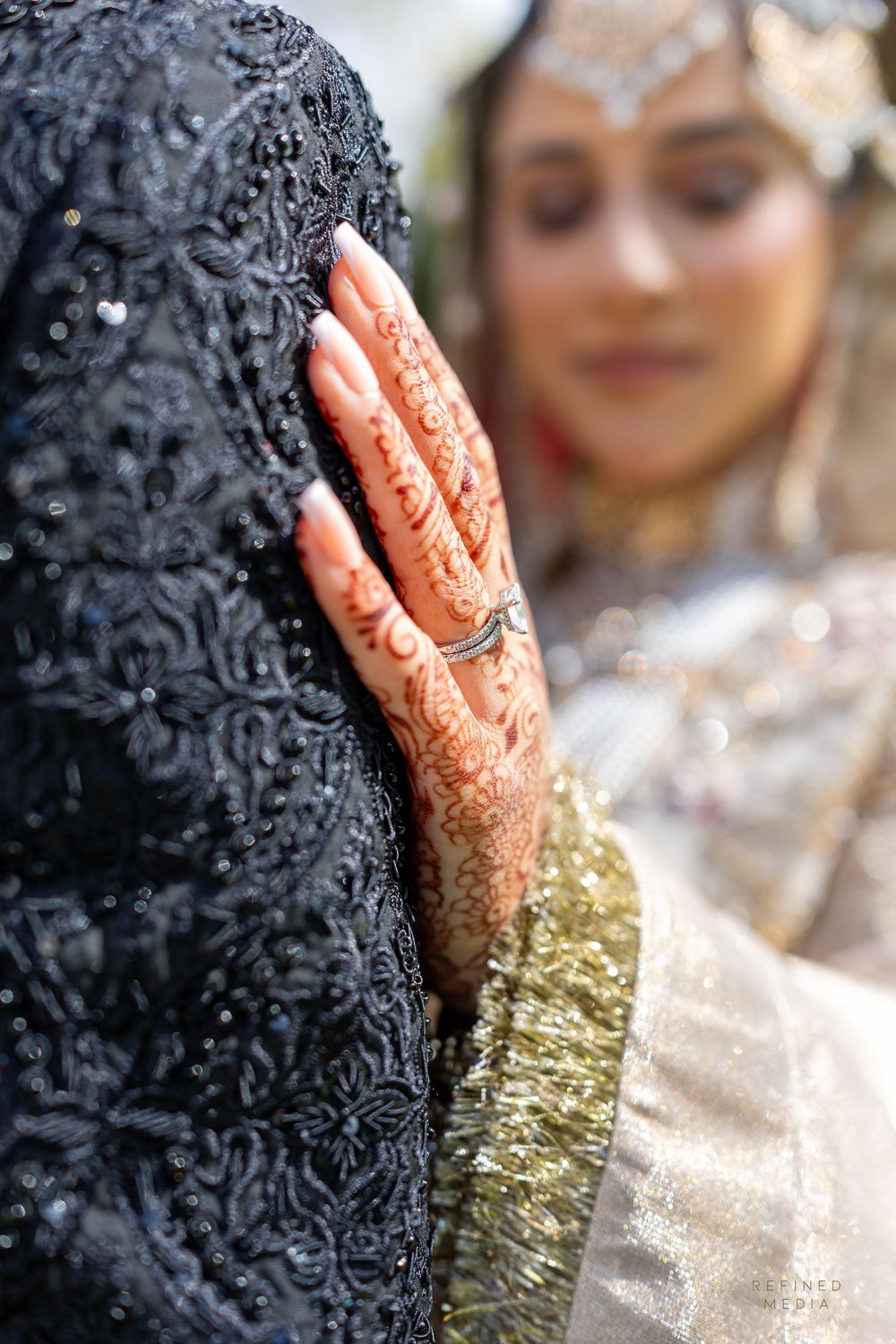 A hand adorned with henna and jewelry rests on a glittery gold and silver surface creating an elegant bridal detail shot.