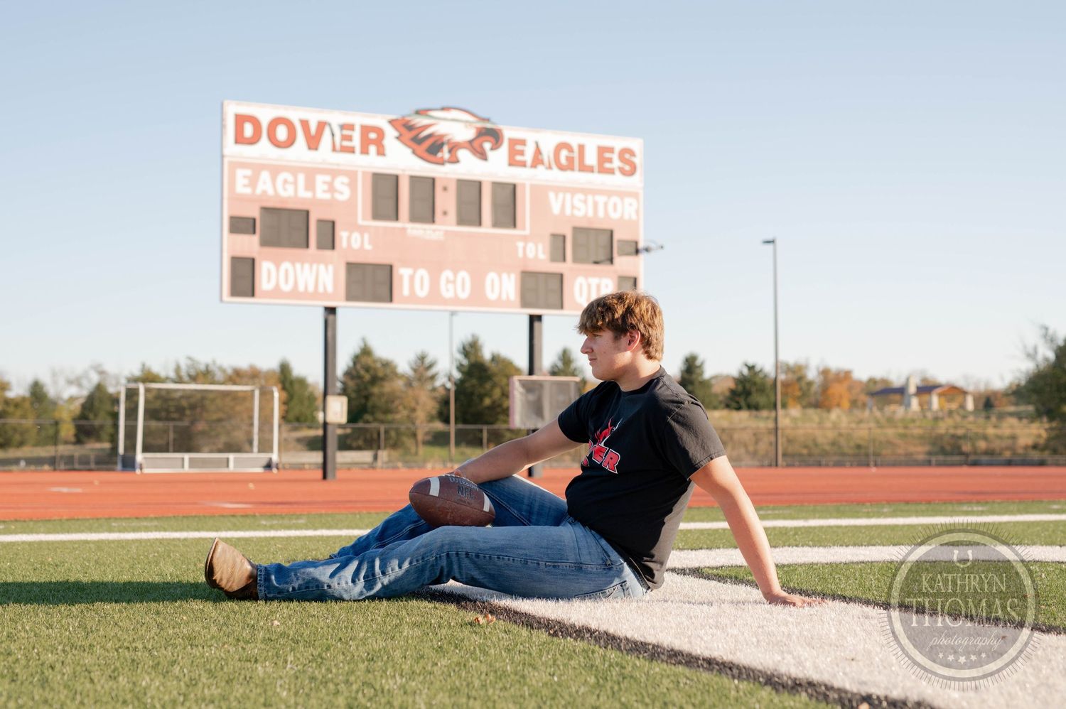 Athlete poses casually by Dover Eagles scoreboard on football field at sunset.