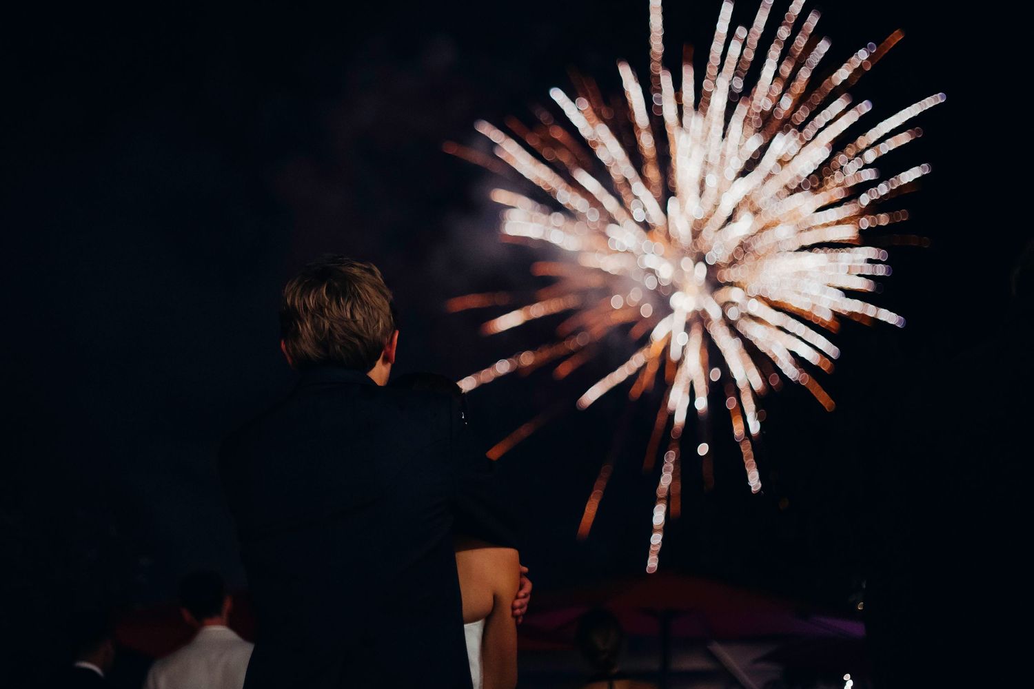 Person watching a spectacular burst of colorful fireworks lighting up the dark night sky.