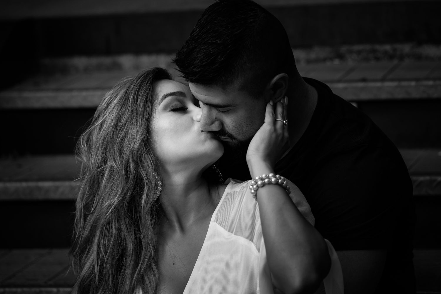 An intimate black and white portrait of a couple sharing a tender romantic moment in muted lighting.