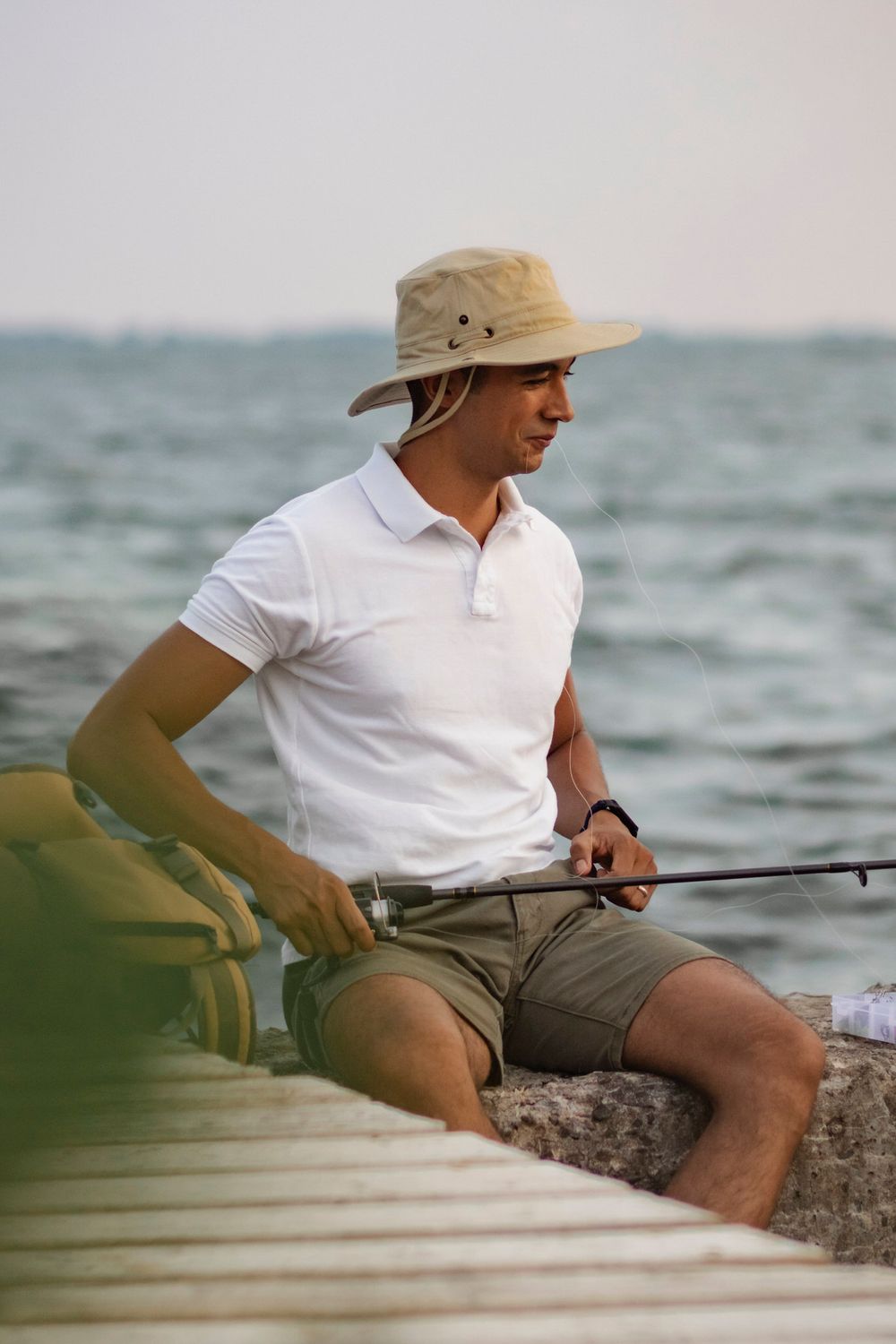 Man sits on the breakwall of Lake Ontario, preparing to fish.