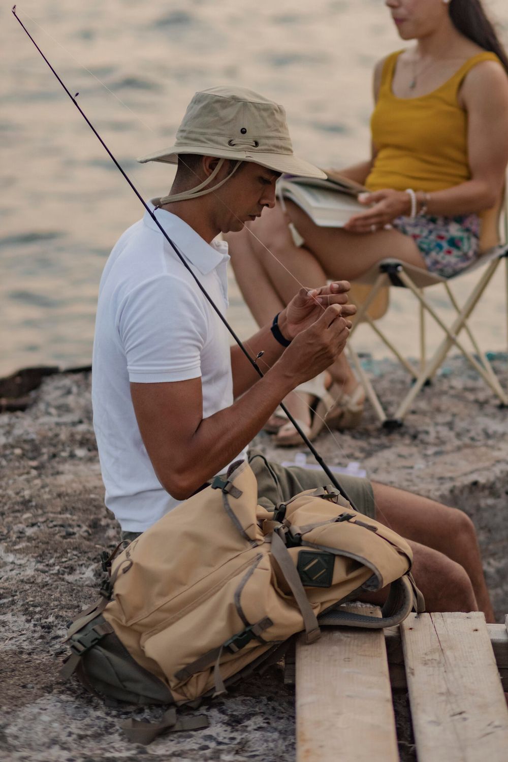 Couple sits on a breakwall of Lake Ontario preparing to go fishing. He baits his hook while she sits in a lawn chair and reads. Kingston, ON