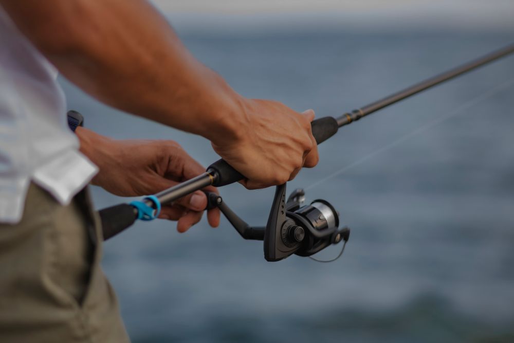 Man fishes from the shoreline of Lake Ontario. Detail of his hands reeling the rod.