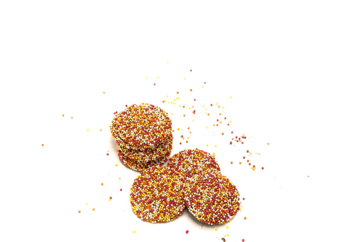 "Een stapeltje ronde chocolaatjes met felgekleurde sprinkles eroverheen, verspreid over een witte achtergrond. Lekker en feestelijk!"