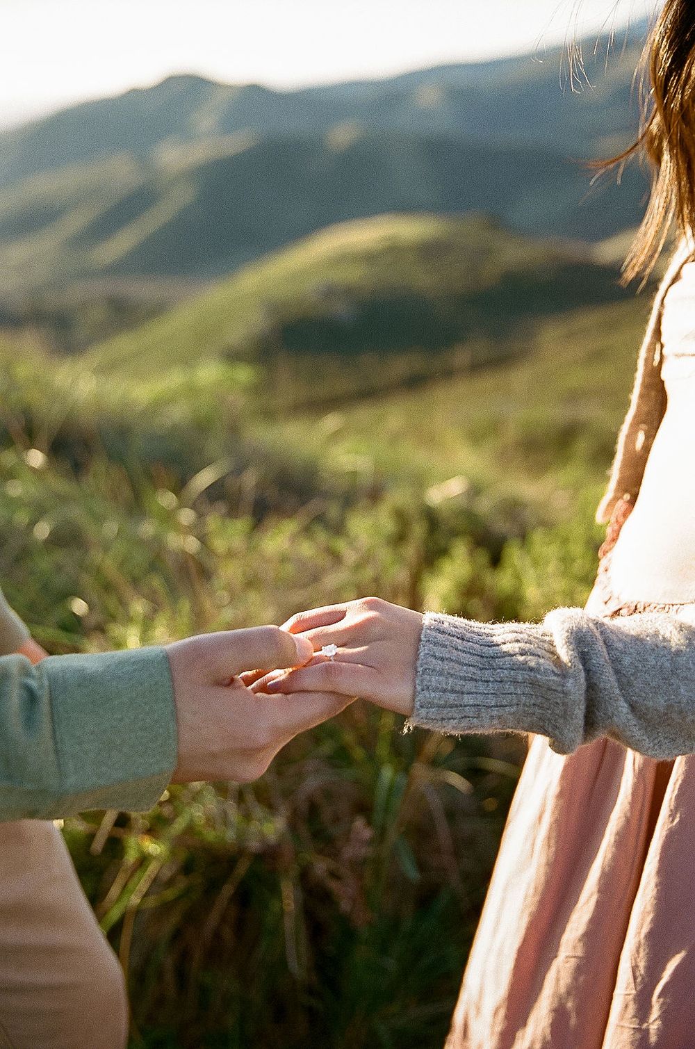 Close-up of hands with an engagement ring against a backdrop of scenic mountain landscapes.