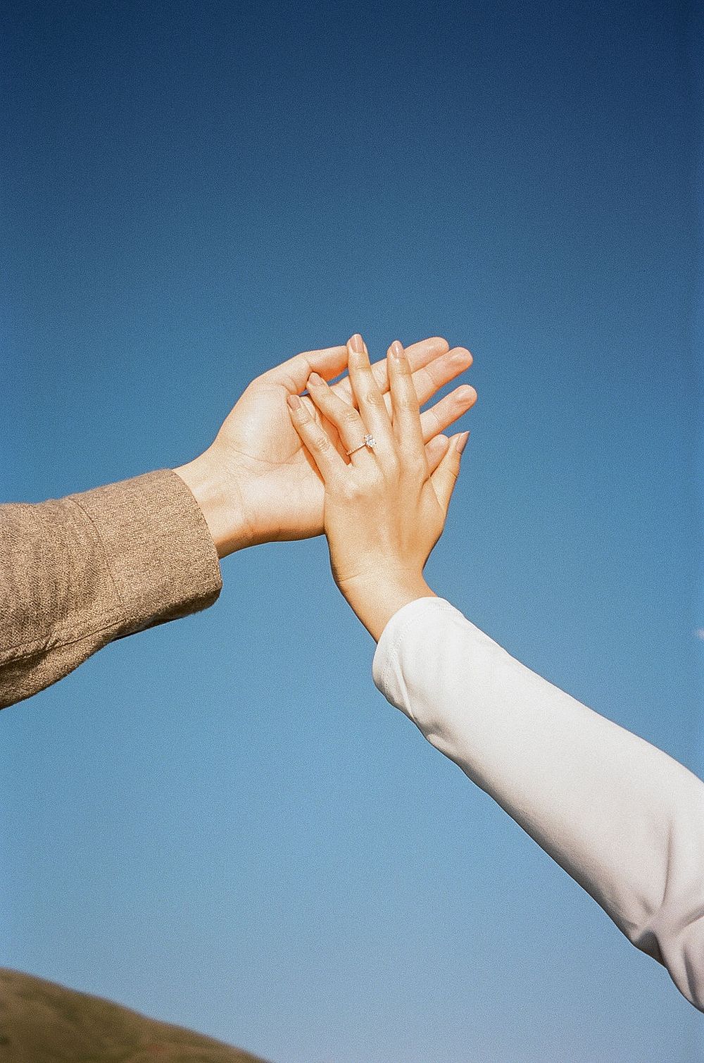 Two hands reach out and touch against a bright blue sky in a symbolic gesture of connection.