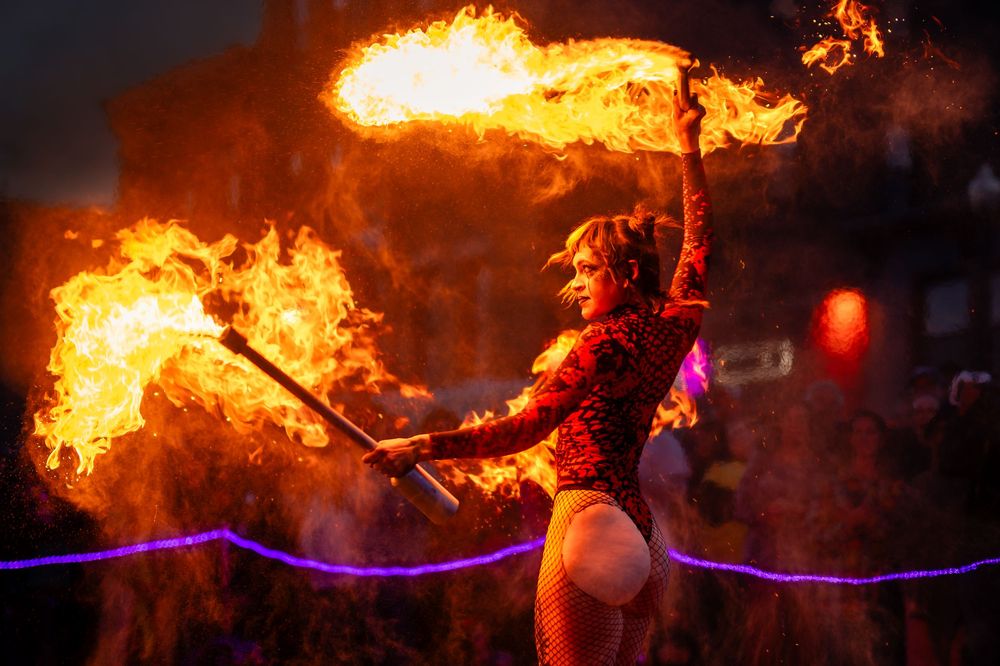 Fire performer twirls flaming batons in a dramatic nighttime display of fire dancing and performance art.