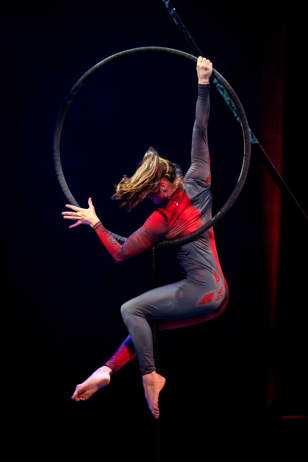 Aerial performer in red and black attire gracefully moves through a series of dynamic poses on a suspended hoop.