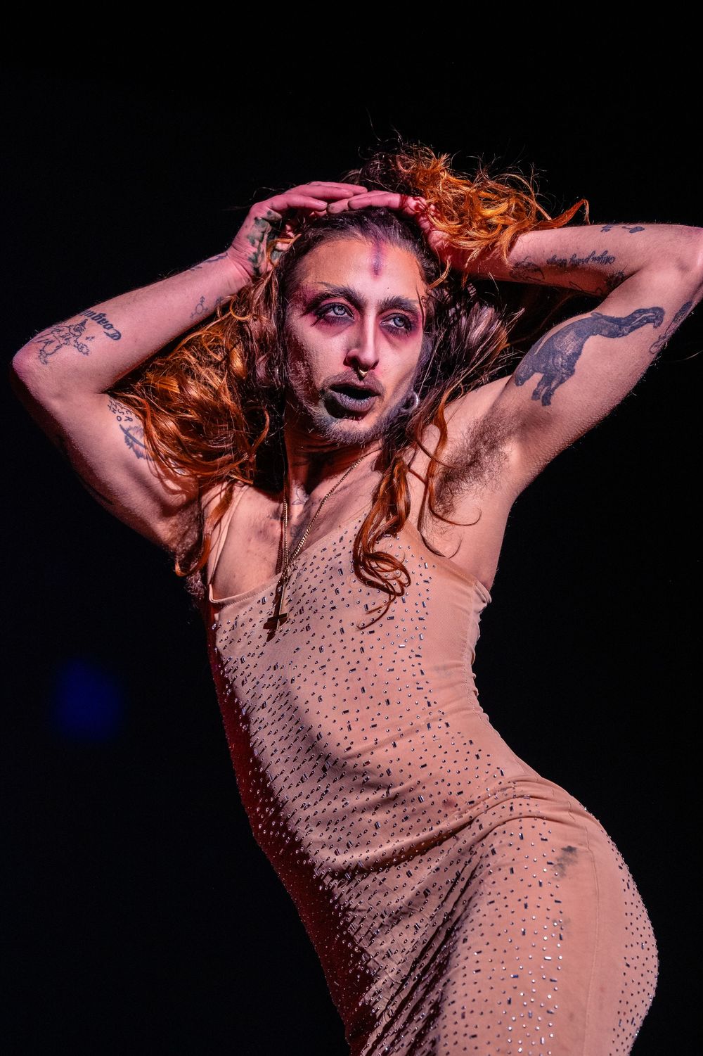 A performer in a sparkly top dances expressively with arms raised during a dramatic stage performance.