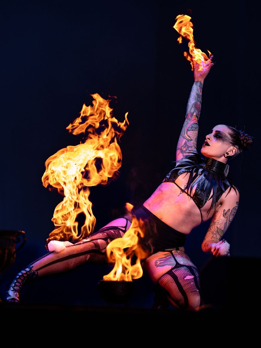 Fire performer creating dramatic flame effects during a dark stage performance with striking orange illumination.