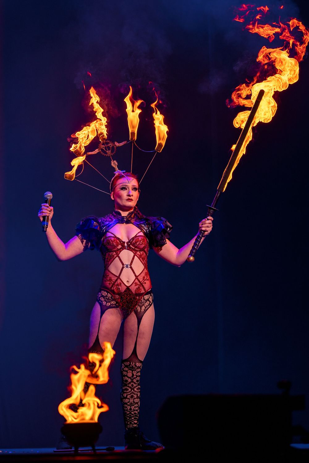 Performer wielding flaming torches in a red costume on stage with dramatic lighting effects.