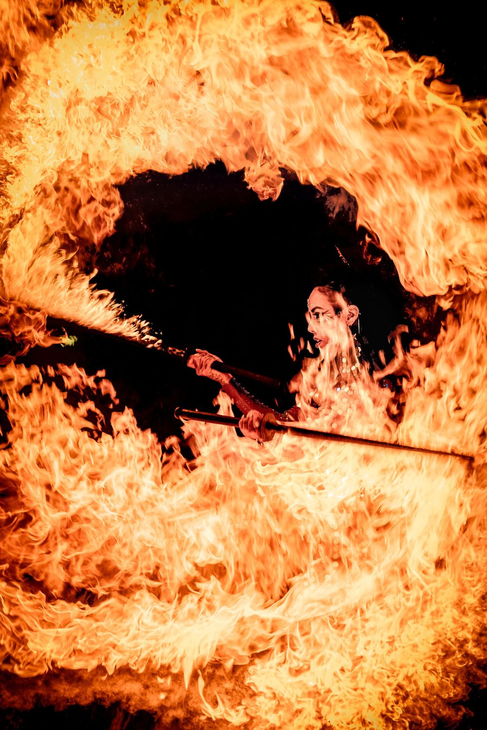 A fire performer manipulates a flaming staff against a dark background creating dramatic swirls of orange flames.