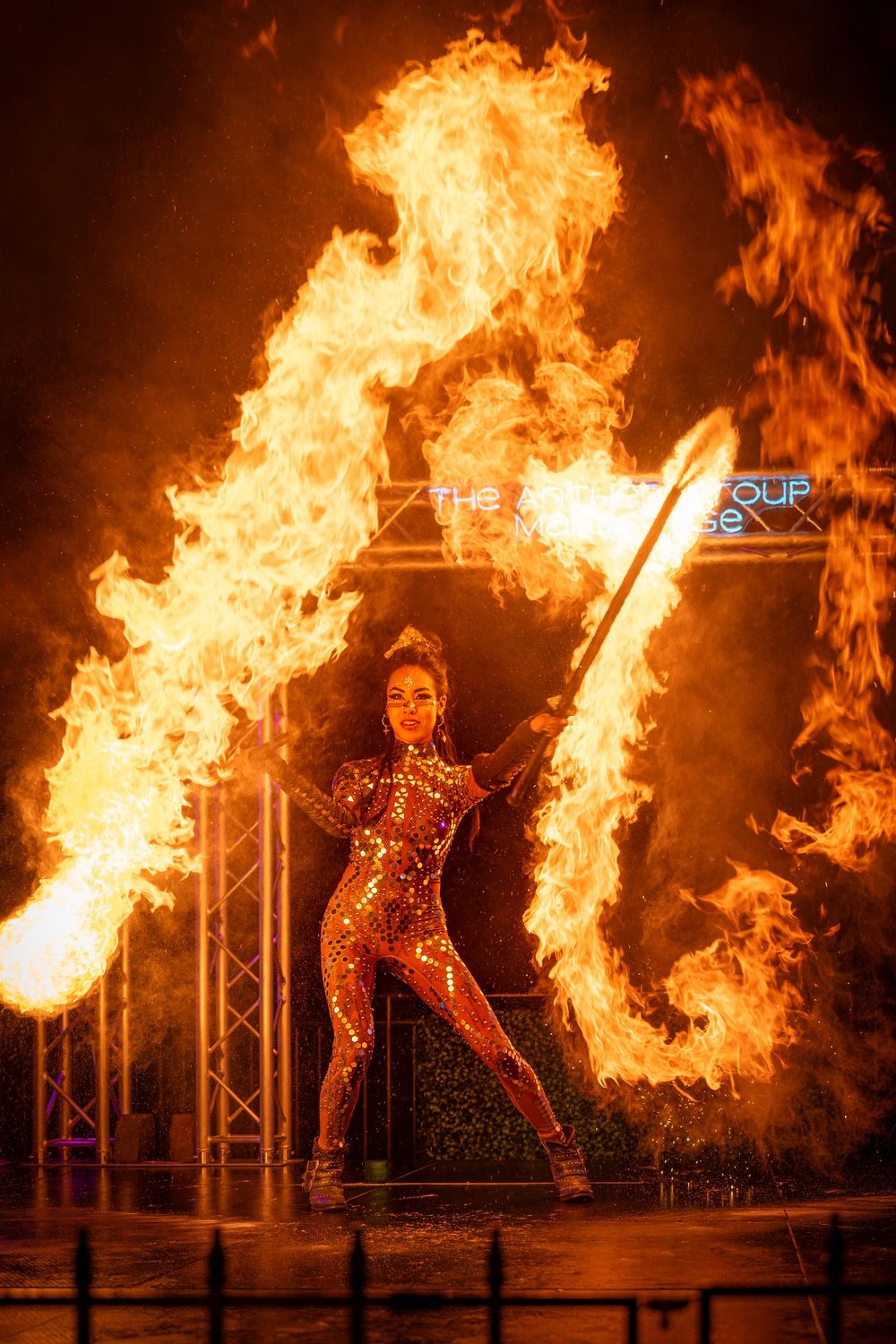 A performer in a sparkly costume manipulates flaming props creating dramatic fire patterns on stage.