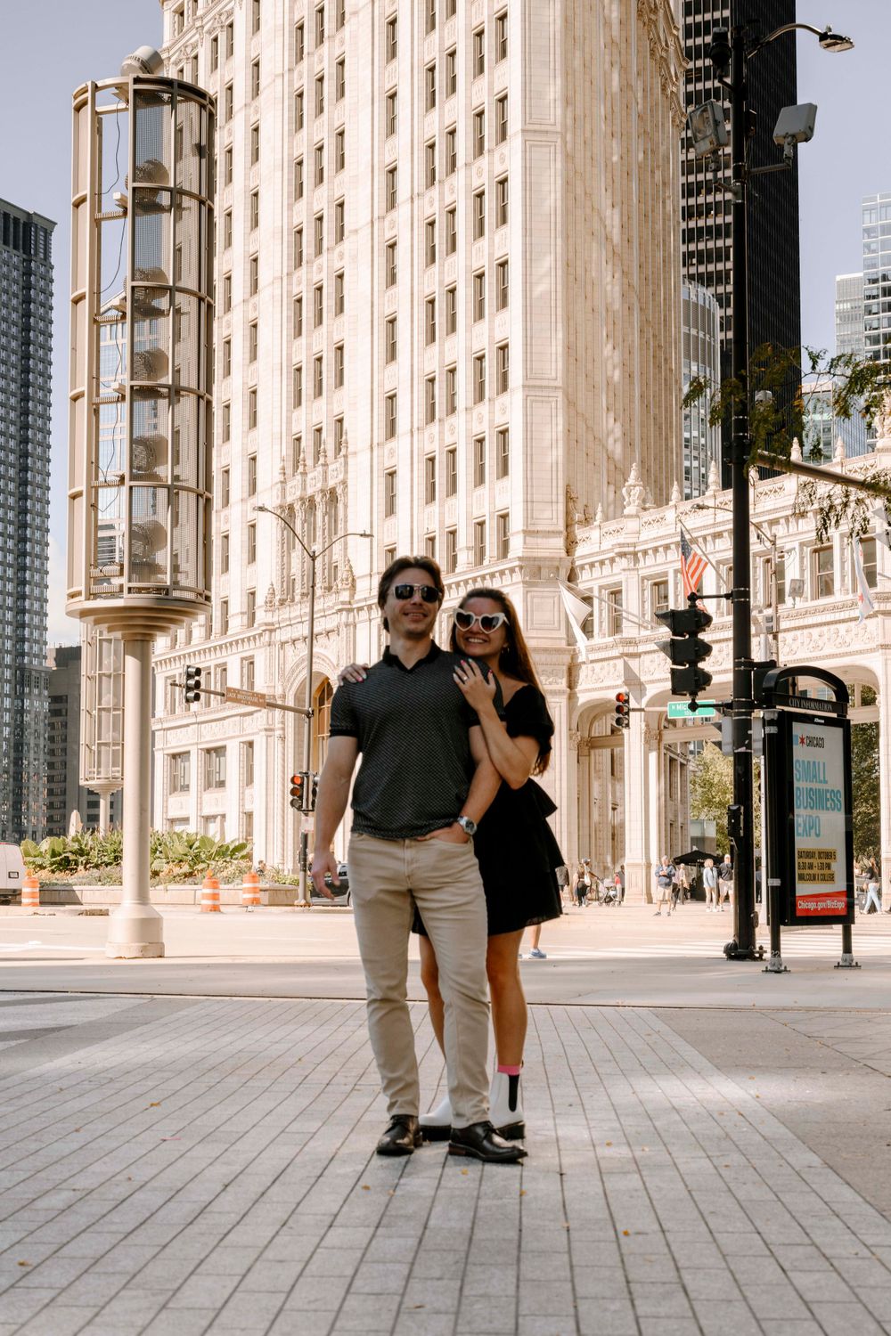 A couple walking together on a city sidewalk near historic architecture and tall buildings in an urban setting.
