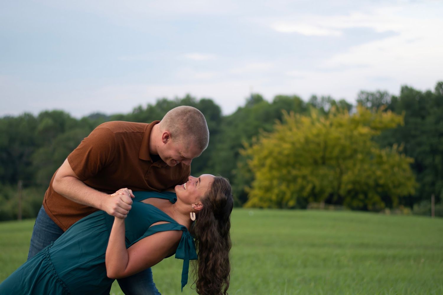 Husband dipping wife and gazing at her lovingly in a sunlit field during golden hour - romantic couples session