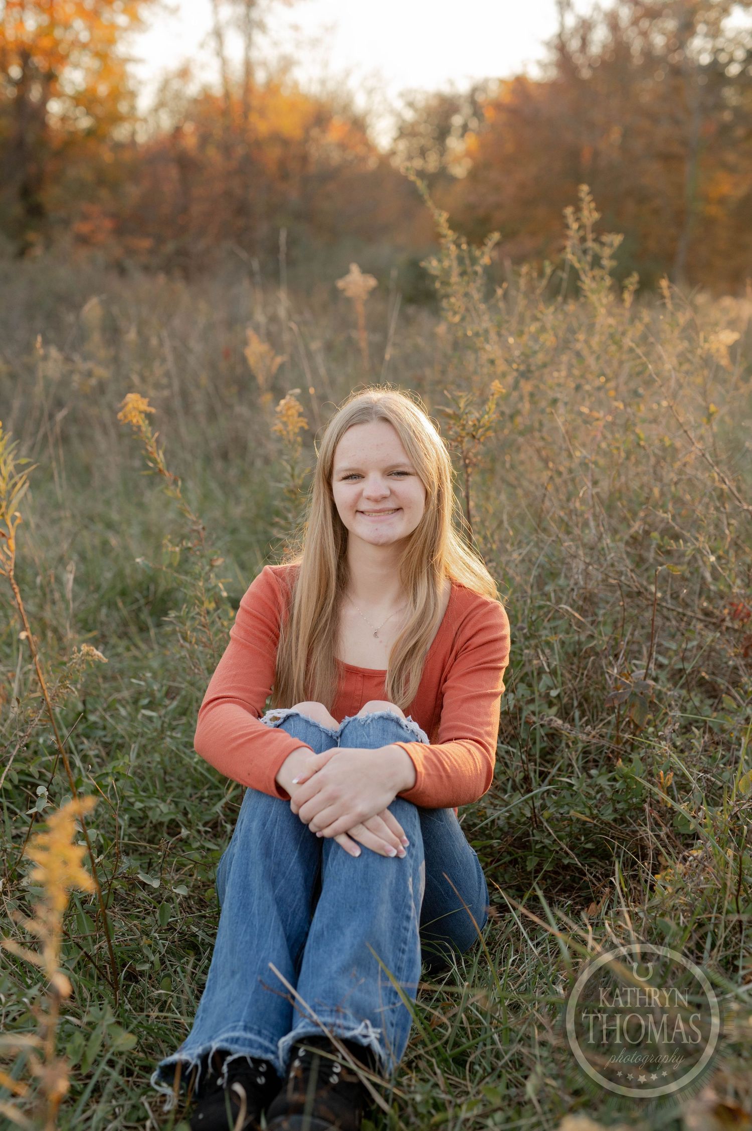 A casual autumn portrait in a field with soft evening light filtering through dried grasses and trees.
