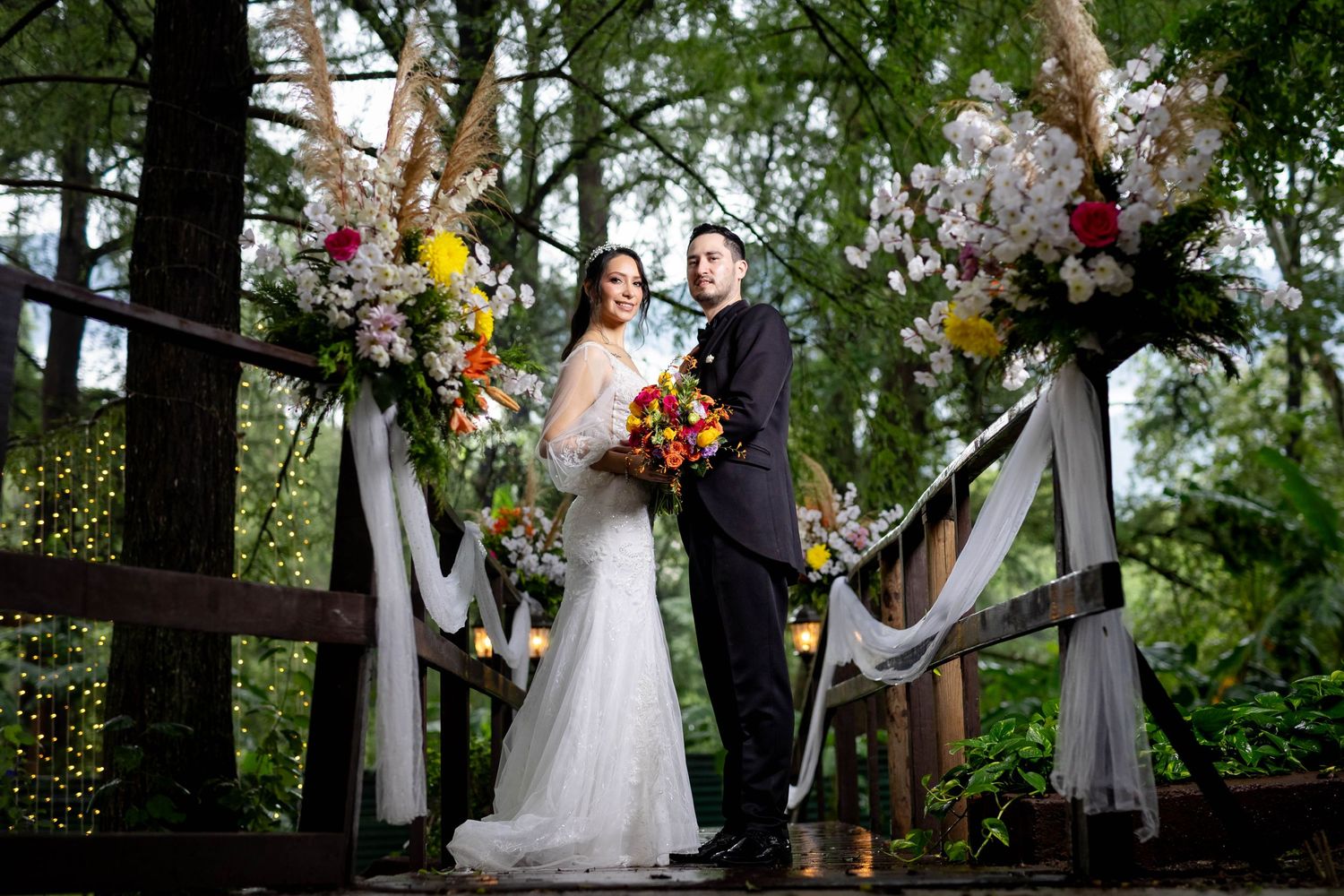 Wedding ceremony setup in forest with white drapes and floral arrangements framing the couple.