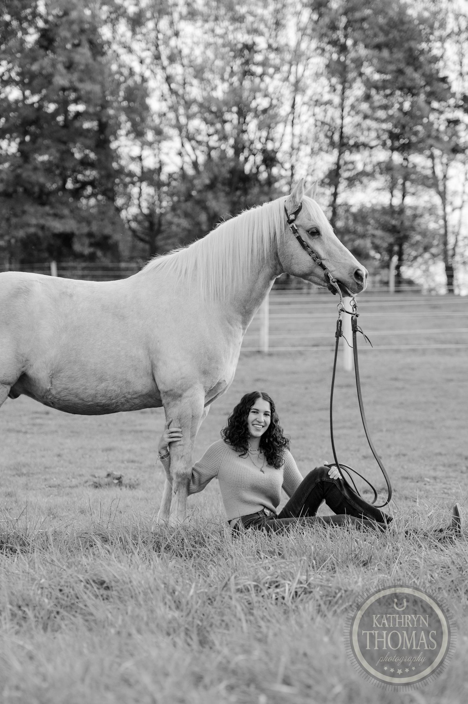 Black and white photo of a serene moment with a white horse and rider relaxing in a grassy field.