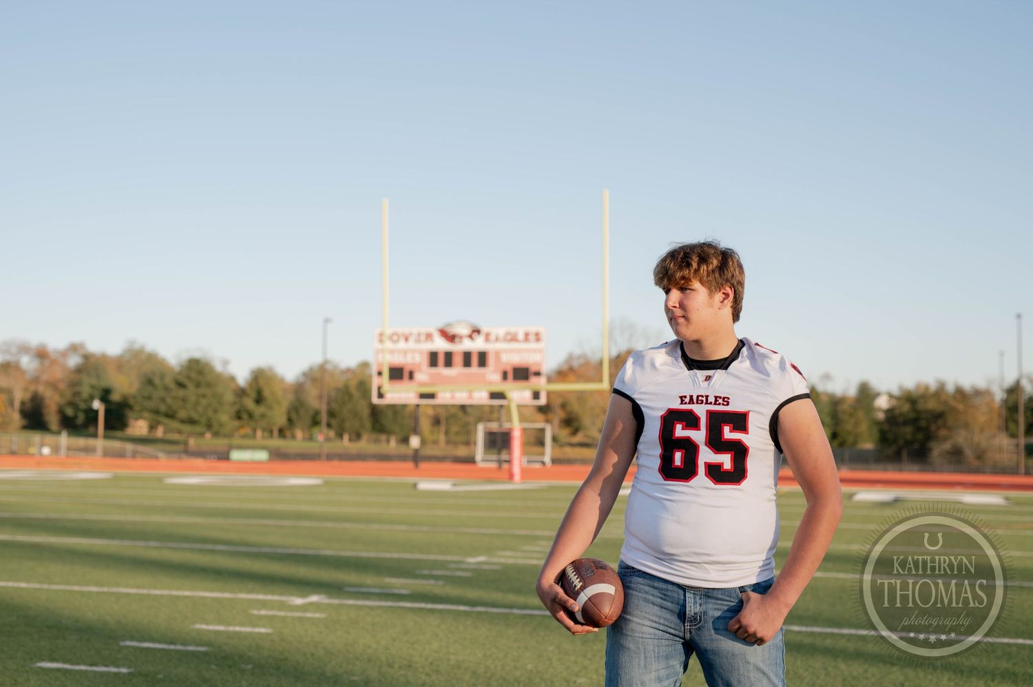 Player in white jersey holds football on field with Dover Eagles stadium visible behind.