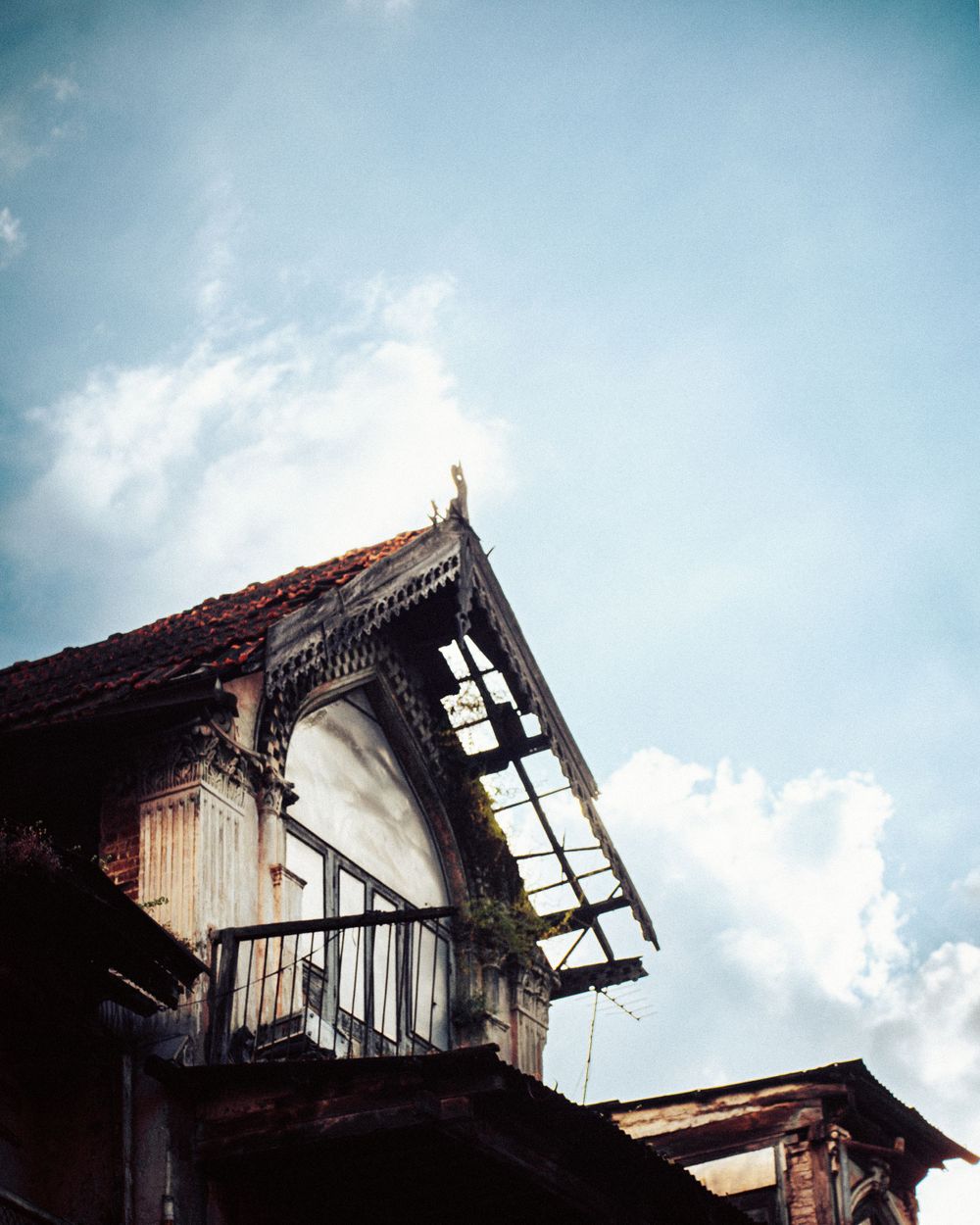 Dilapidated building exterior with broken windows and exposed structural elements against blue sky.