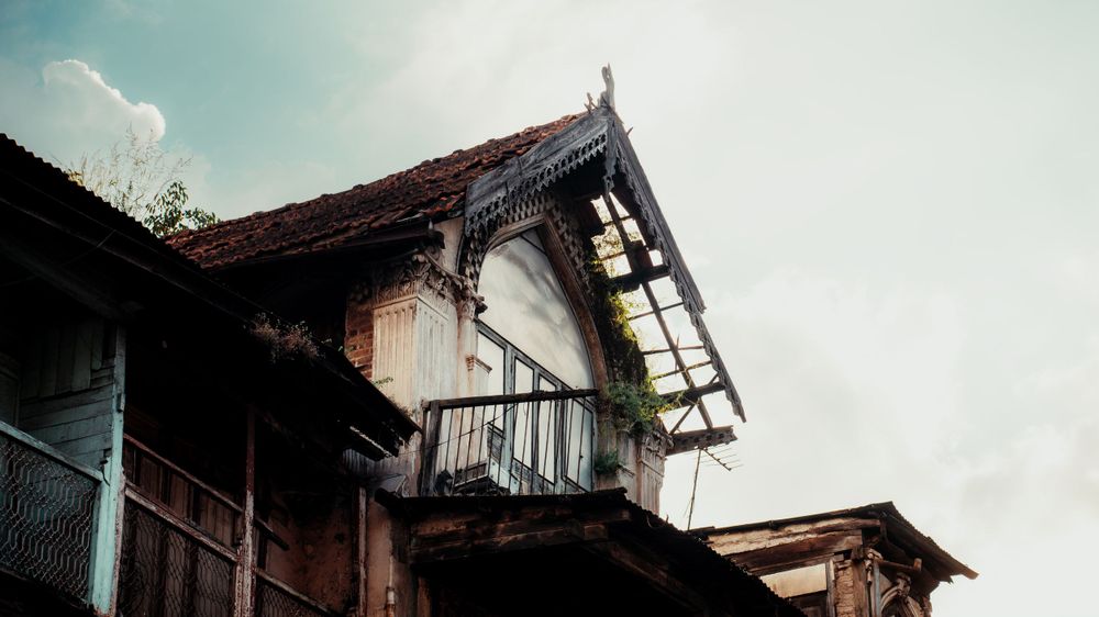 Weathered architectural details of an old building's upper floor against bright sky.