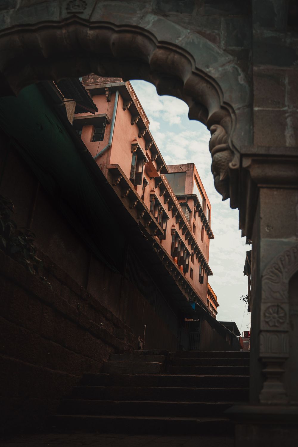 Ancient stone architecture with ornate arches framing a terracotta-colored building against blue sky.