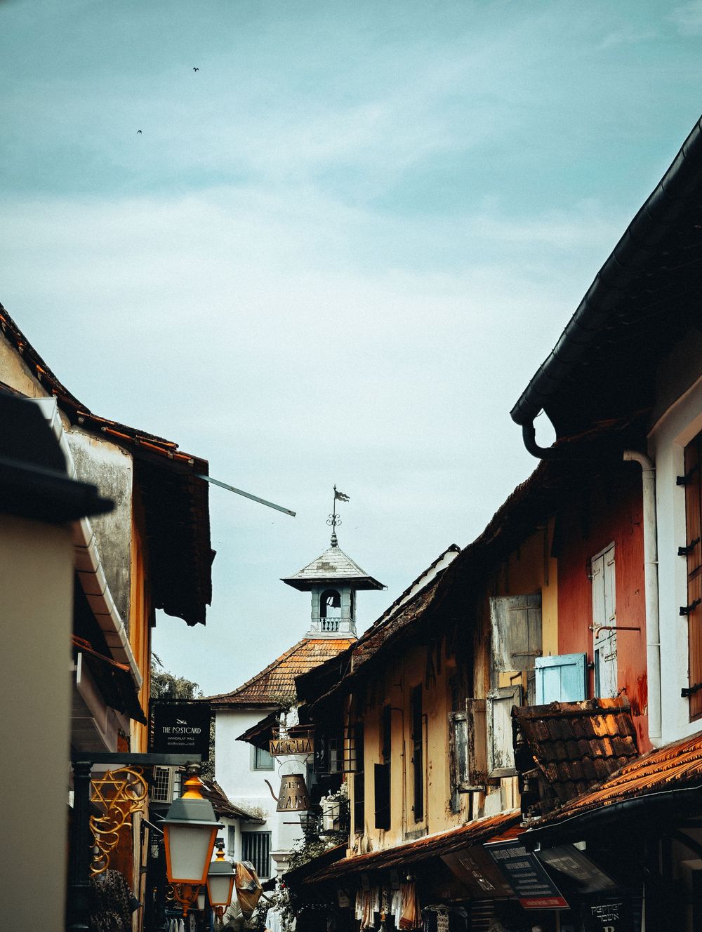 Historic European village street with traditional architecture and church bell tower against blue sky.