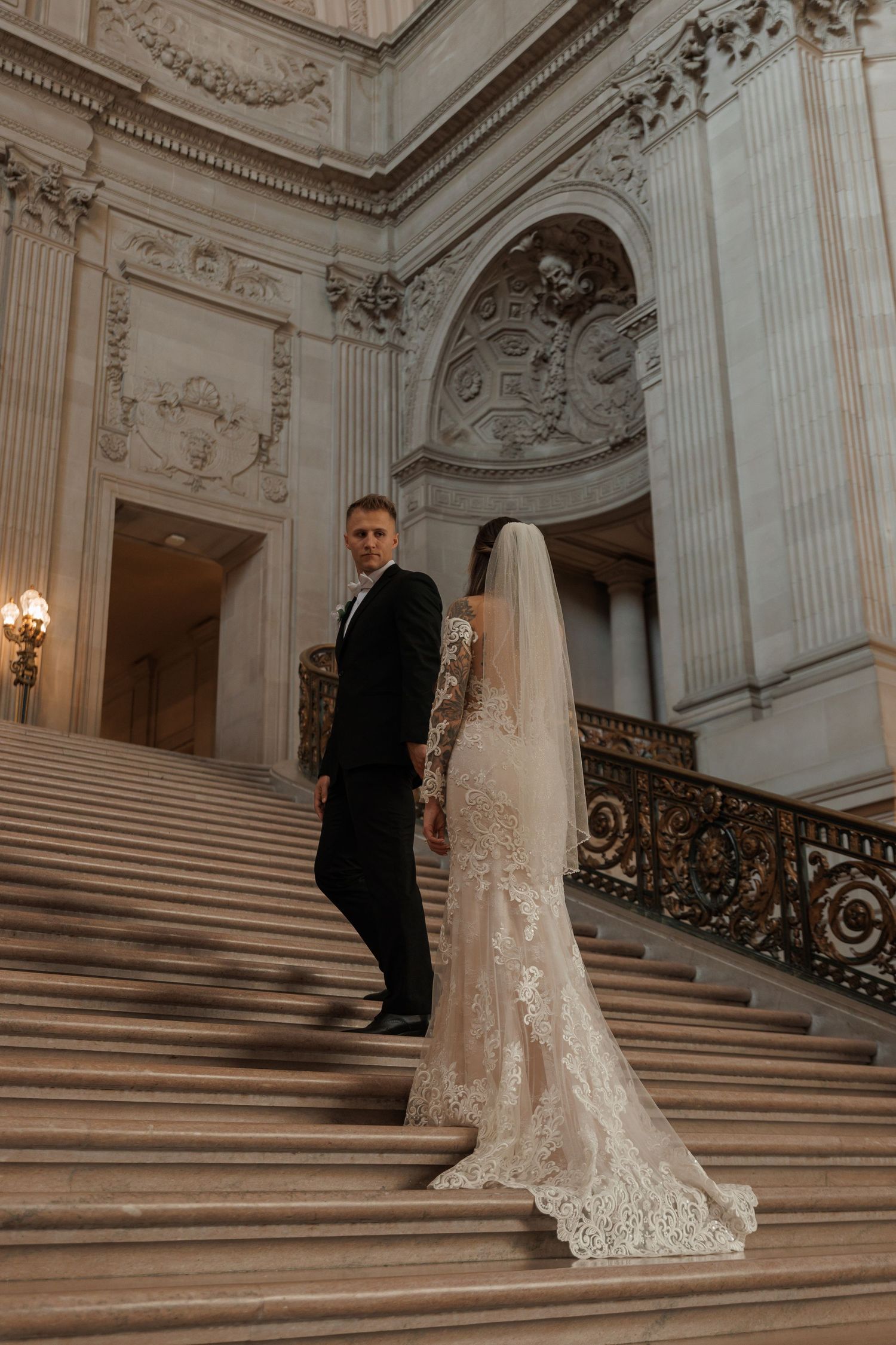 Newlywed couple poses on ornate marble staircase in San Fransisco City Hall with classical architecture details.