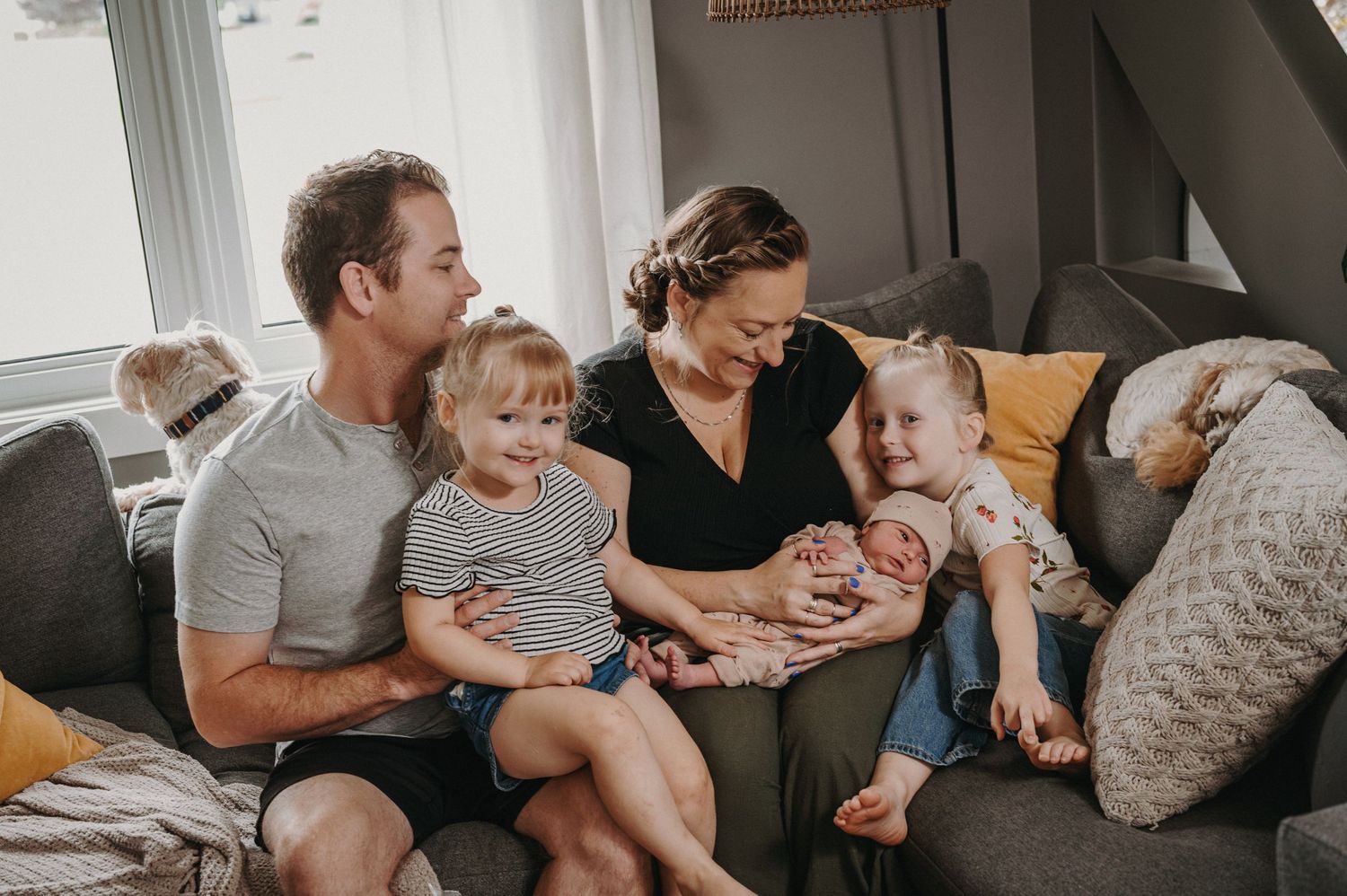 Family relaxing together on gray couch during casual in-home lifestyle session.