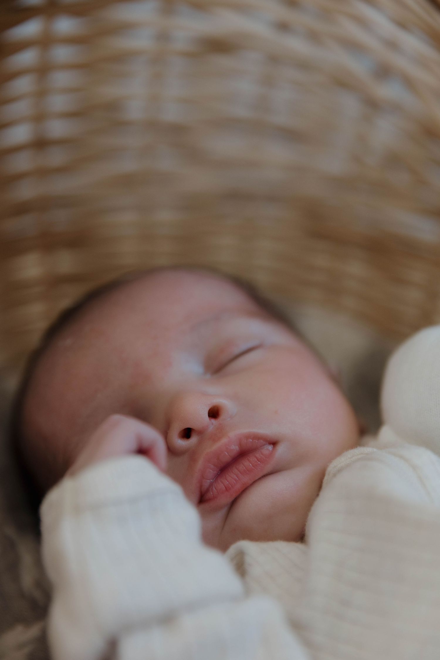 A peaceful sleeping baby nestled in a cozy white blanket and wicker bassinet.