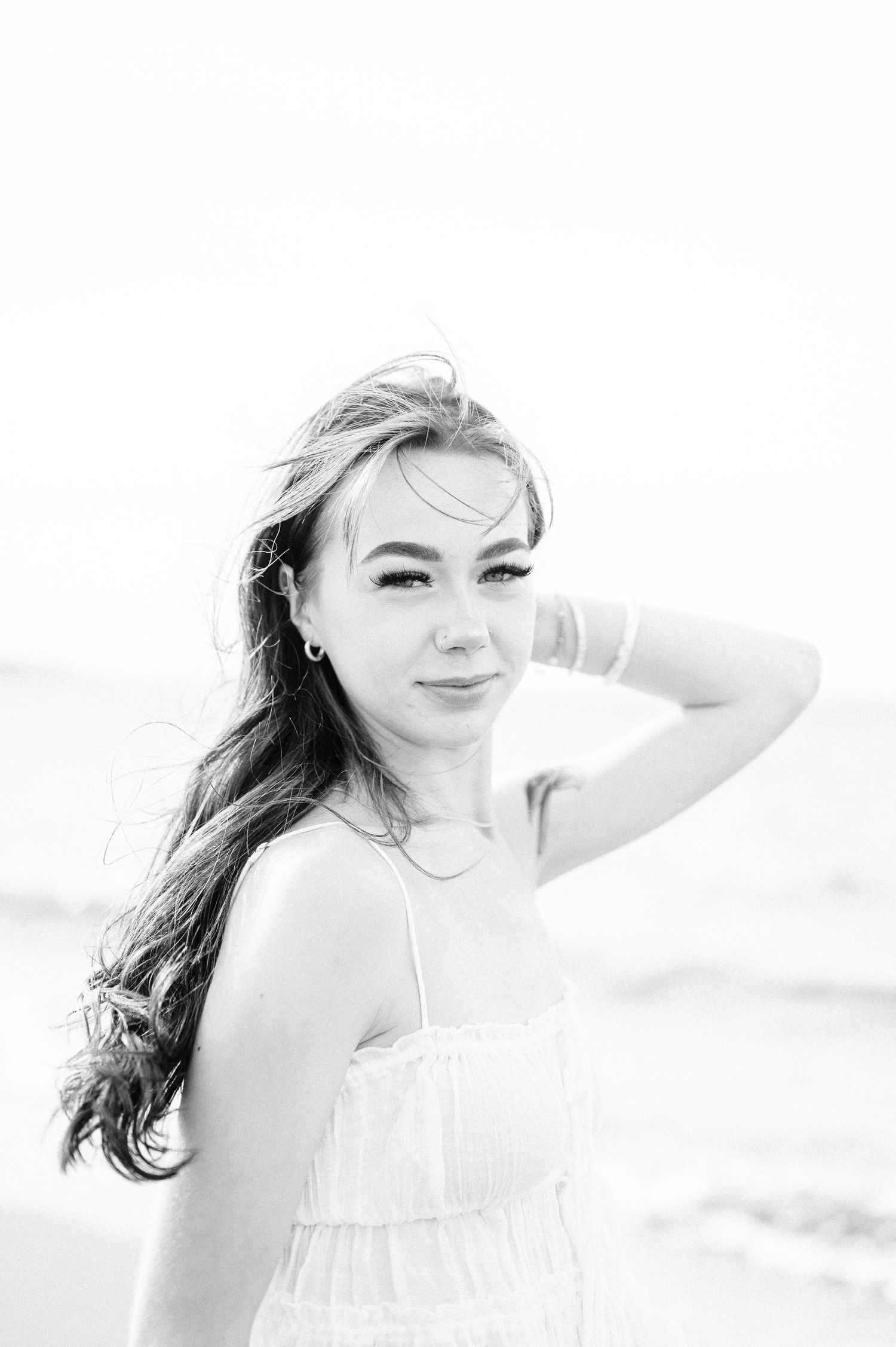 A girl in a white dress poses outdoors in a bright setting with wind-swept hair. Photo by Bremerton Senior Portrait Photographer.