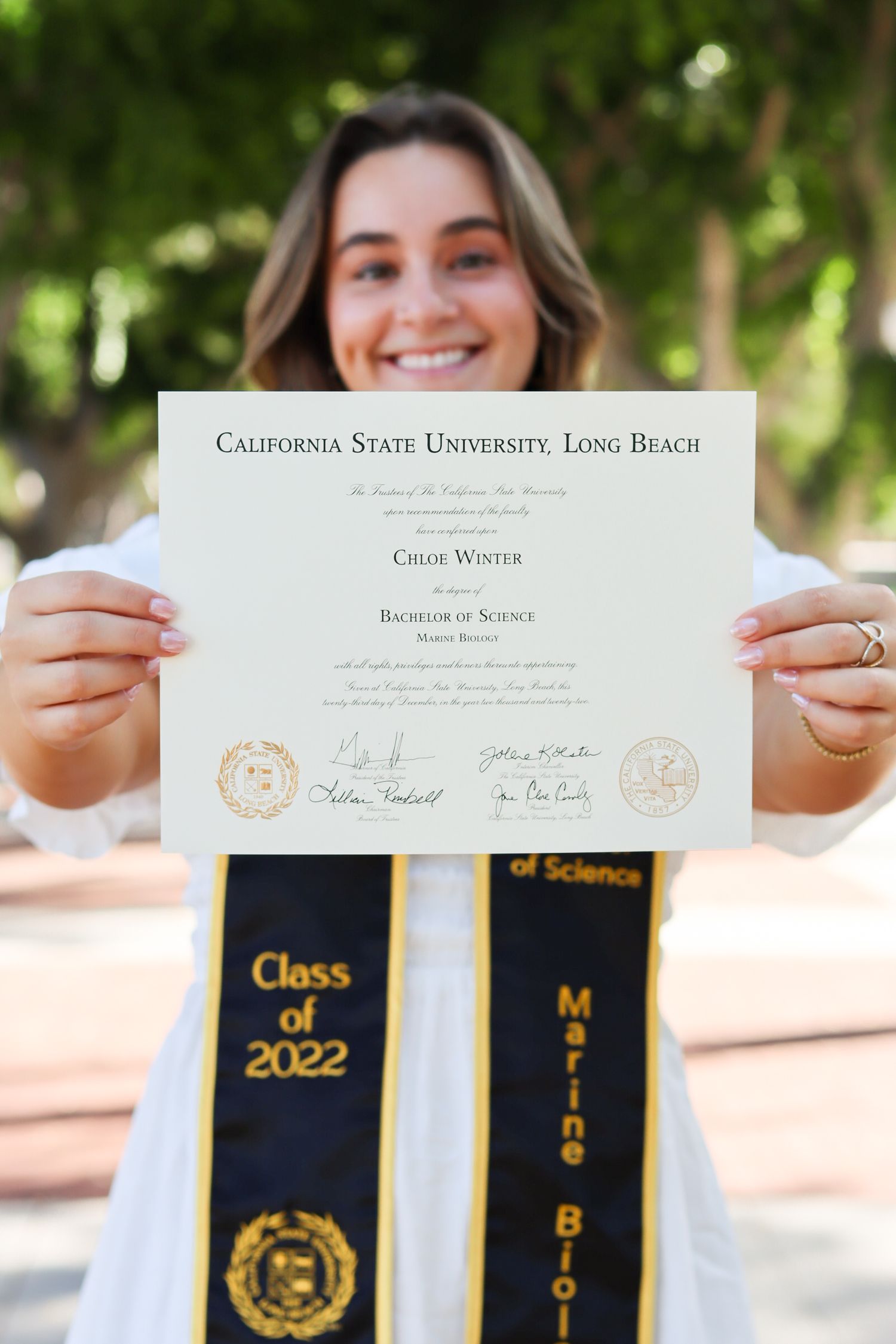 Graduate displaying Cal State Long Beach diploma with Class of 2022 graduation stoles.