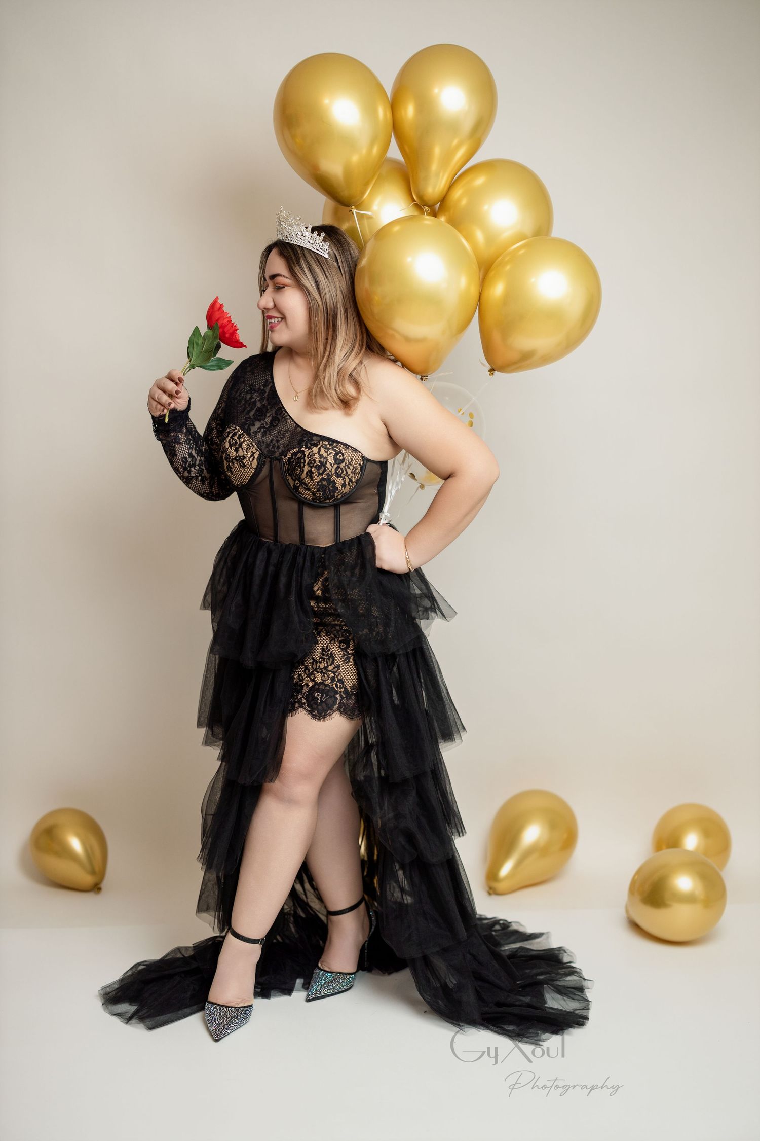 A glamorous pose with gold balloons and a black lace dress while holding a red rose.