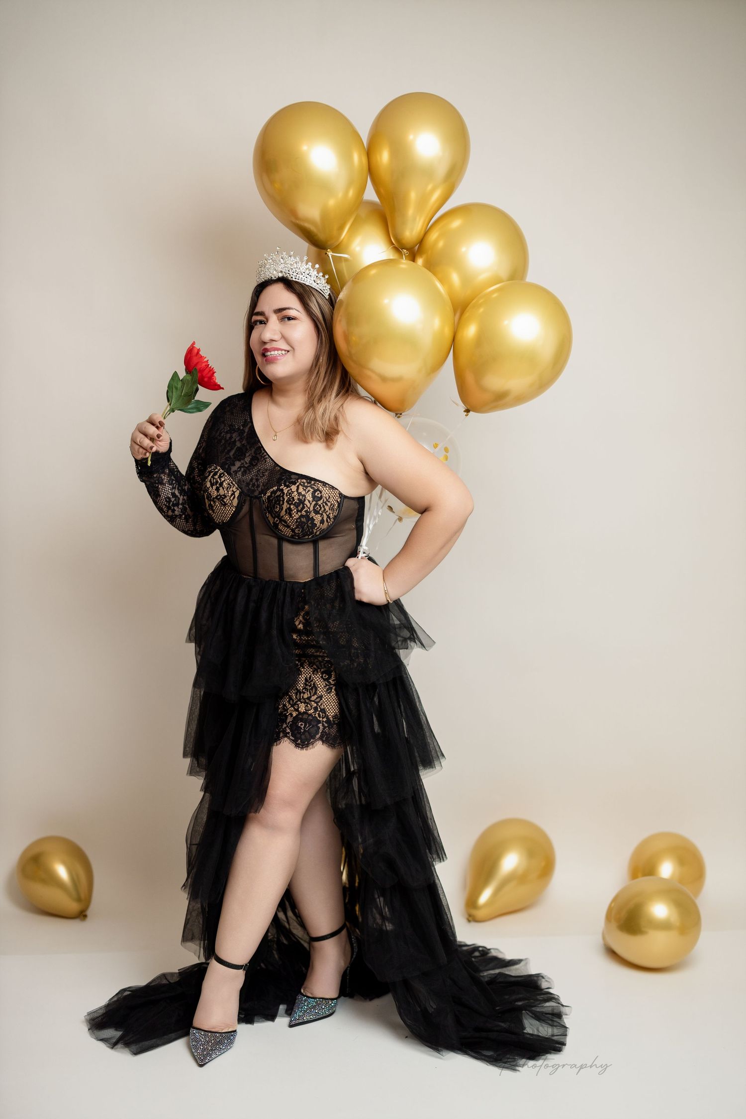 A joyful pose in a black lace dress with golden balloons and a red rose.