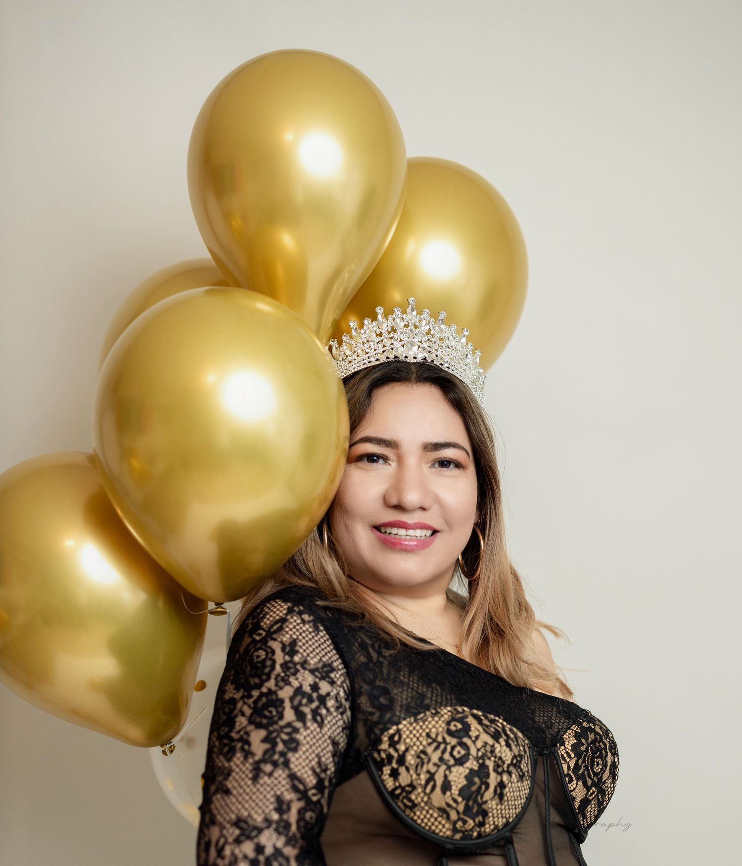 An elegant portrait with gold balloons and a crystal crown against a neutral background.